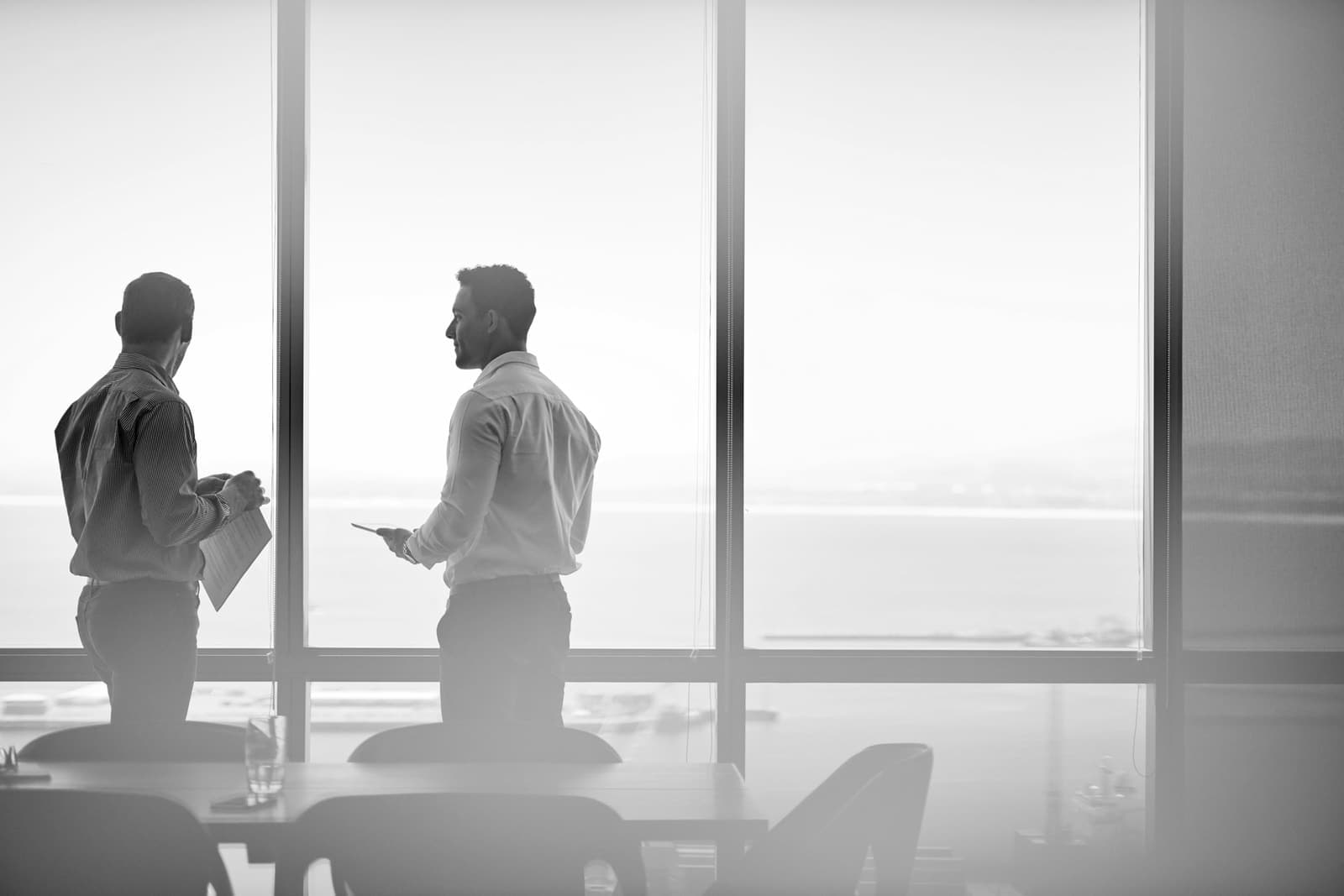 Two executives in conversation at the panoramic window of an office tower